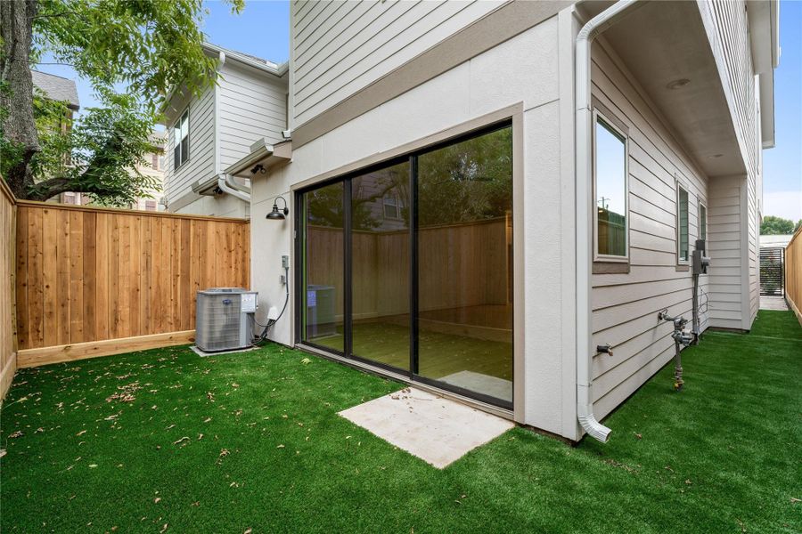 Private side courtyard — low-maintenance artificial turf, privacy fencing, direct glass sliding door access, and covered exterior entry.