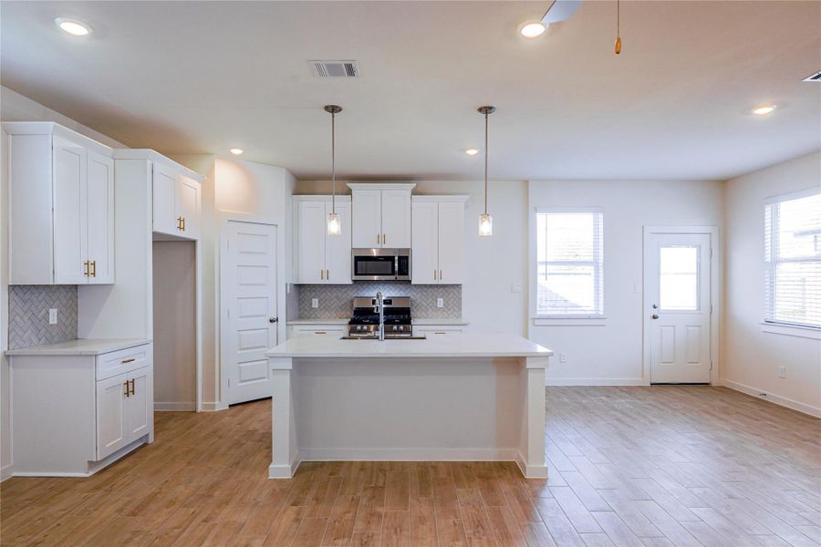 Modern kitchen with white cabinetry, a central island, and stainless steel appliances. The open layout features wood-look flooring, ample natural light, and a herringbone backsplash. Perfect for cooking and entertaining.