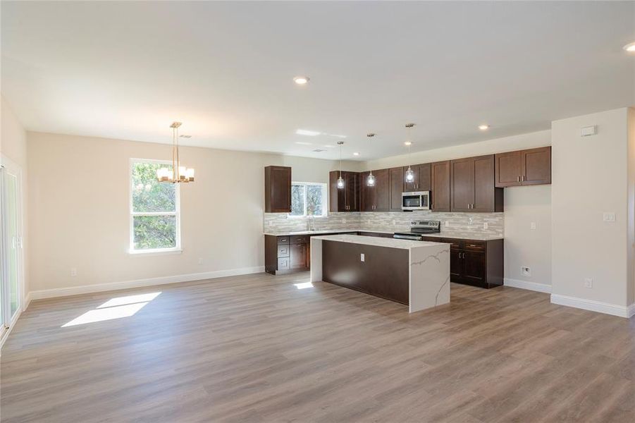 Kitchen featuring light wood-type flooring, hanging light fixtures, a center island, and stainless steel appliances