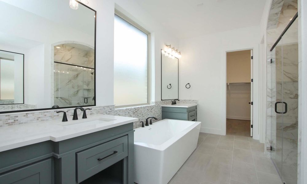 Bathroom featuring a marble finish shower, two vanities, a freestanding bath, and a walk in closet