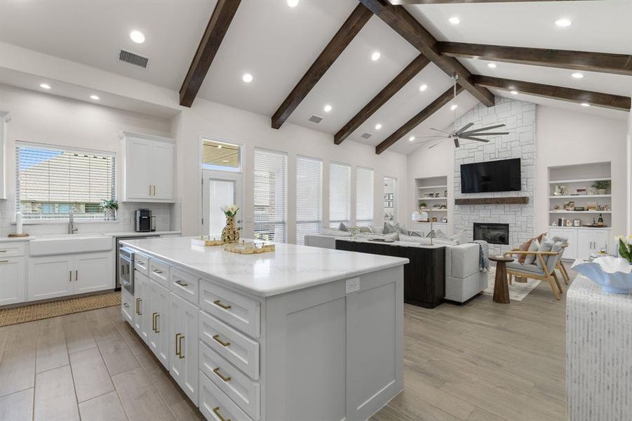 Kitchen featuring white cabinetry, a stone fireplace, a kitchen island, open floor plan, and light wood-style floors Kitchen featuring white cabinetry, a stone fireplace, a kitchen island, open floor plan, and light wood-style floors