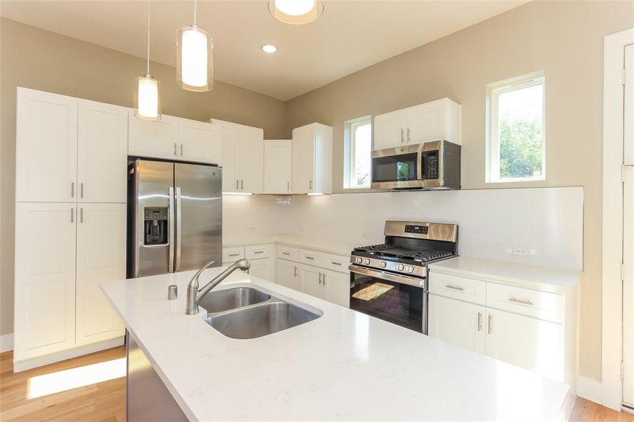 Kitchen with hanging light fixtures, appliances with stainless steel finishes, sink, and white cabinets