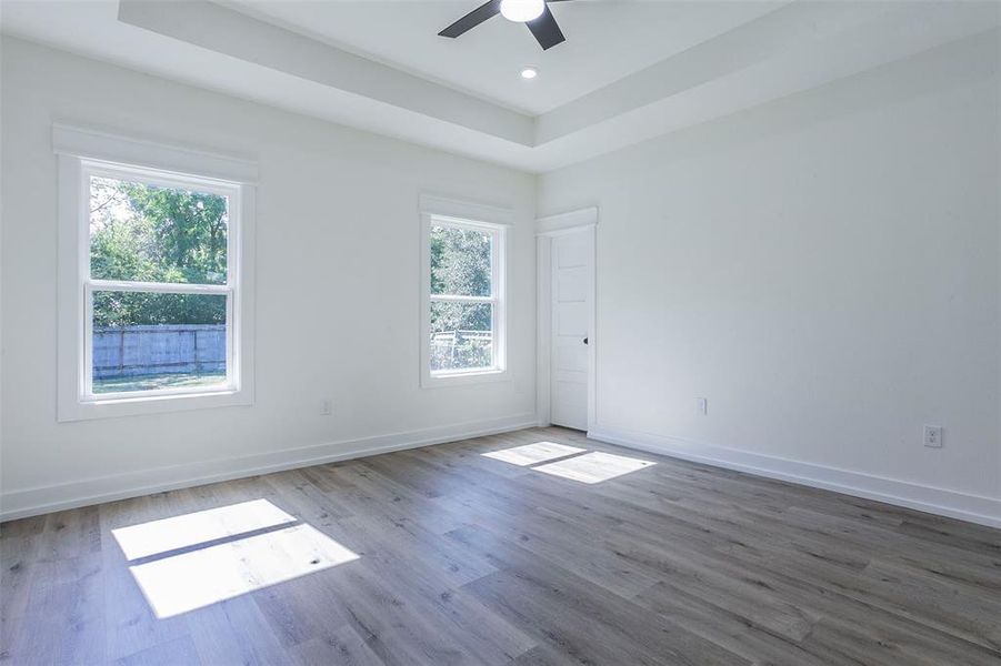 Room with wood-finish flooring, white walls, and a tray ceiling