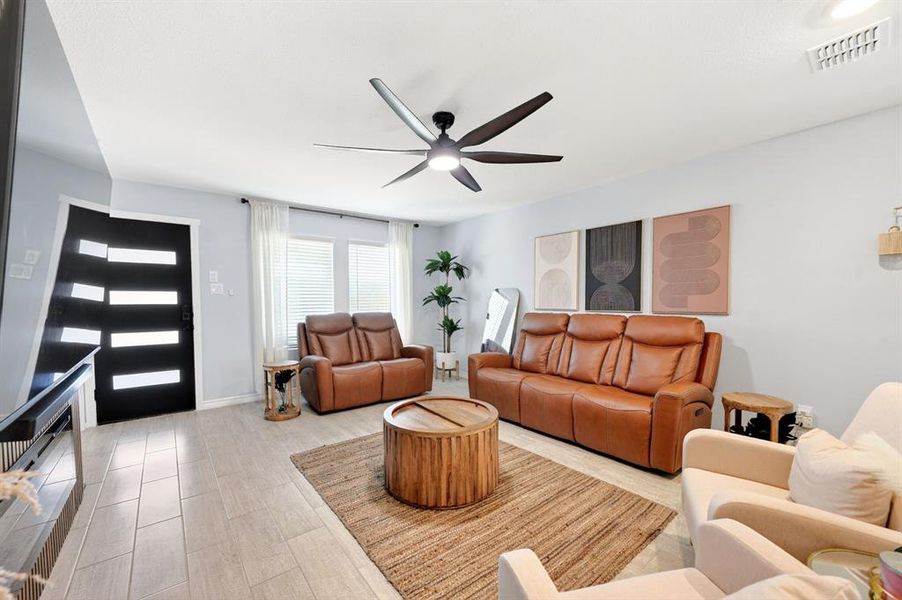 Spacious living area featuring light-toned tile flooring, light blue walls, and a contemporary ceiling fan