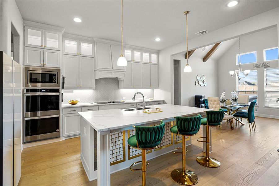 Kitchen featuring glass insert cabinets, tasteful backsplash, white cabinetry, light wood-type flooring, and a breakfast bar Kitchen featuring glass insert cabinets, tasteful backsplash, white cabinetry, light wood-type flooring, and a breakfast bar