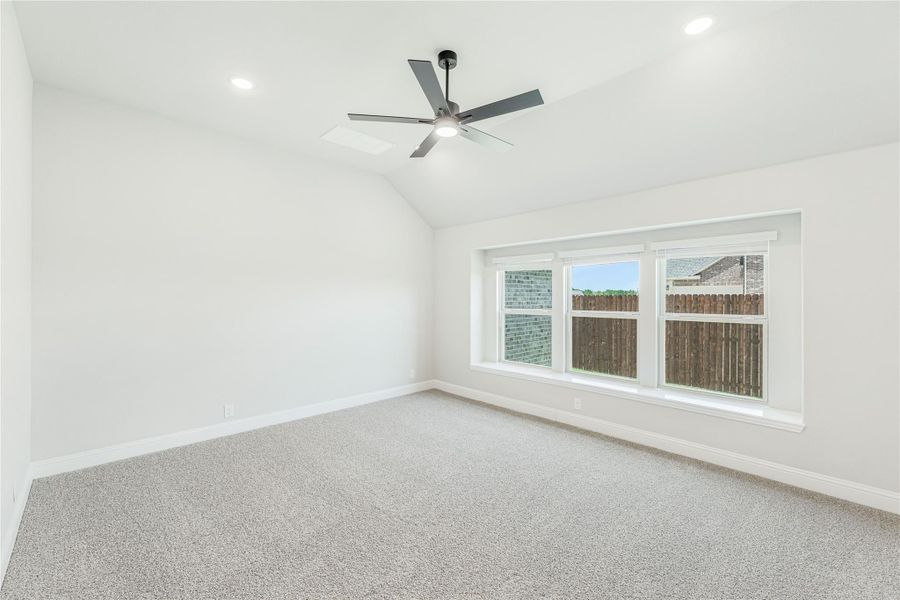 Empty bedroom with vaulted ceiling, ceiling fan, carpet flooring, and large window