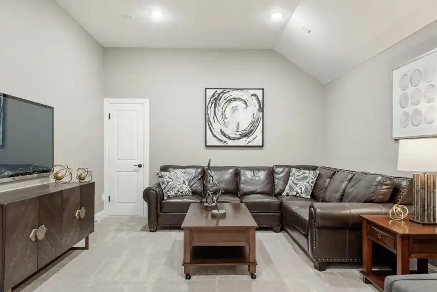 Living room with dark leather sectional sofa, vaulted ceiling, and wall-mounted TV on wood console
