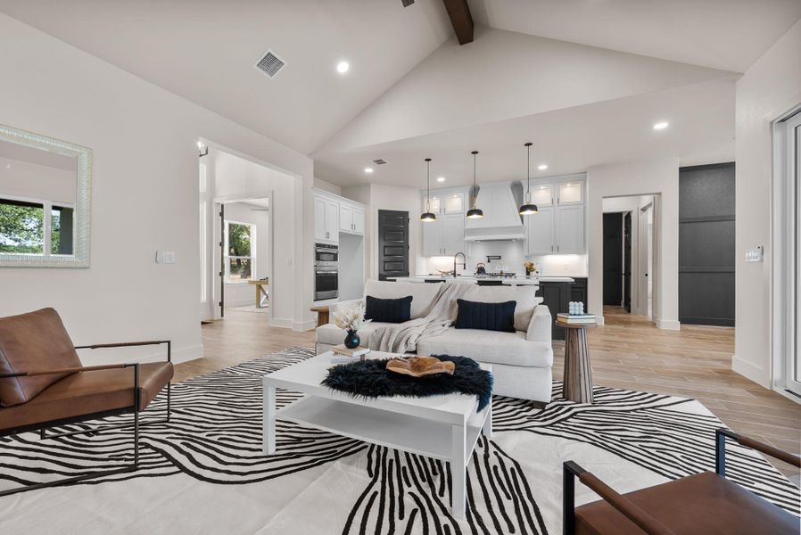 An open concept living area boasts a striking vaulted ceiling and light wood flooring, flowing seamlessly into a well-appointed kitchen.