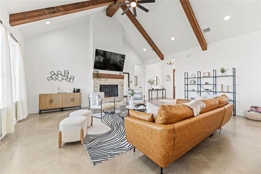Living area featuring concrete flooring, beamed ceiling, high vaulted ceiling, a fireplace, and ceiling fan Living area featuring concrete flooring, beamed ceiling, high vaulted ceiling, a fireplace, and ceiling fan