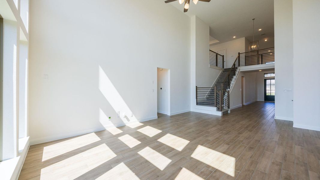 Unfurnished living room featuring a towering ceiling, light wood-style flooring, stairway, recessed lighting, and ceiling fan Unfurnished living room featuring a towering ceiling, light wood-style flooring, stairway, recessed lighting, and ceiling fan