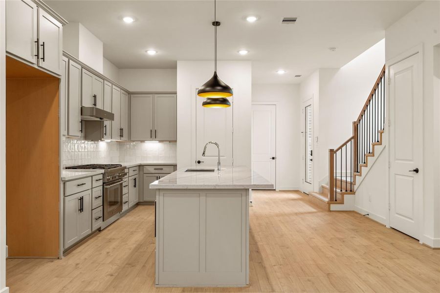 Heart of the main level — centered island prep station, wide-plank oak flooring, and direct sightlines to the stair run and entry foyer.