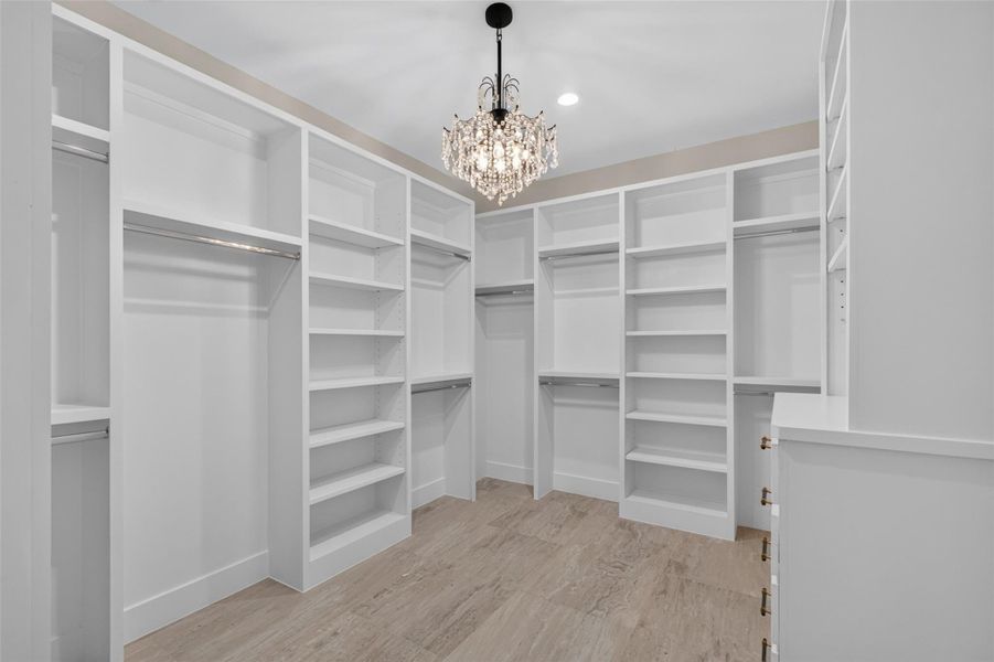 Elegant walk-in closet featuring custom shelving, ample hanging space, and a stunning chandelier, offering both luxury and functionality.
