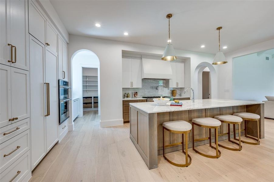 Kitchen with arched walkways, light wood-style flooring, a breakfast bar area, custom exhaust hood, and recessed lighting