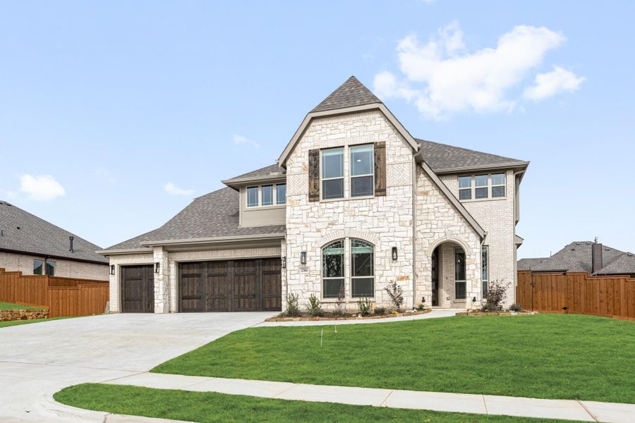 Two-story home with light stone exterior, three-car garage, arched entry, and manicured front lawn
