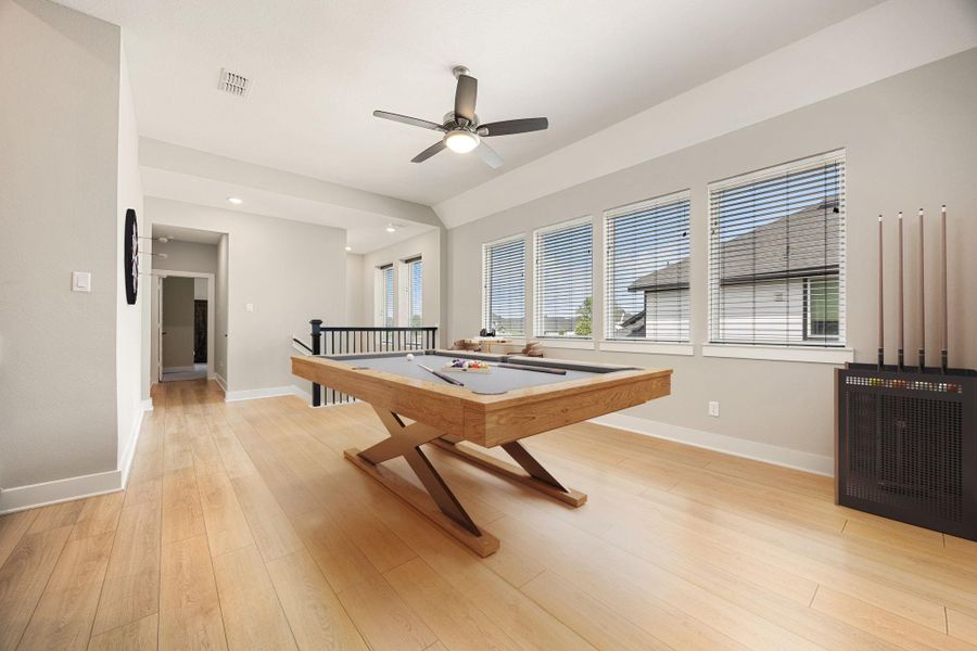 This versatile upstairs game room offers an abundance of natural light through a wall of windows, highlighting the spacious layout and wood-look flooring. Perfectly positioned at the top of the stairs, this open retreat provides the ideal space for relaxation or entertainment.