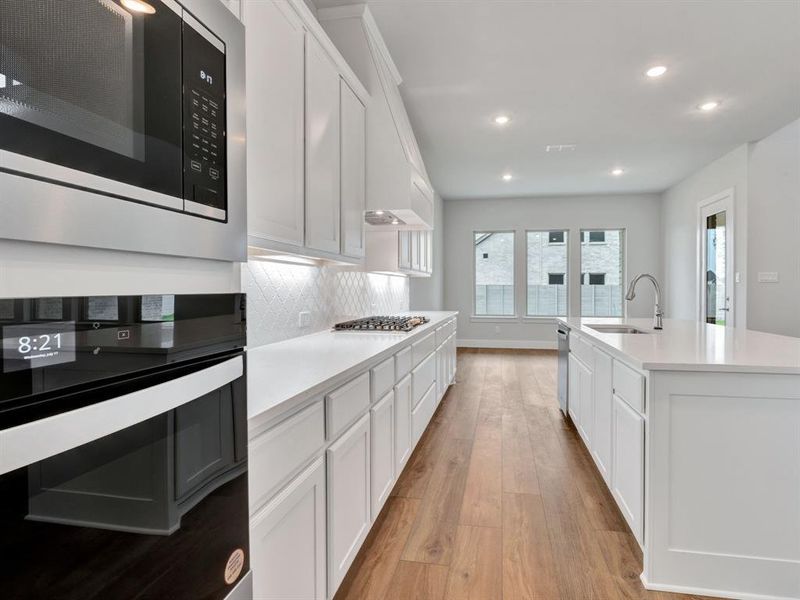 Kitchen with appliances with stainless steel finishes, light wood-type flooring, sink, a center island with sink, and white cabinets