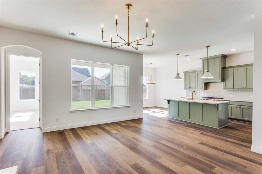 Kitchen featuring a center island with sink, green cabinets, decorative backsplash, decorative light fixtures, and dark hardwood / wood-style flooring