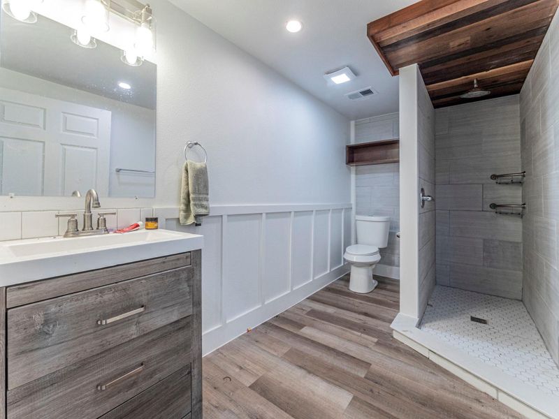 Full bath featuring wainscoting, vanity, a decorative wall, a shower stall, and light wood-style floors