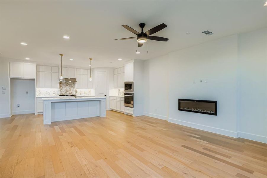 Kitchen featuring white cabinets, decorative backsplash, open floor plan, light wood finished floors, and recessed lighting Kitchen featuring white cabinets, decorative backsplash, open floor plan, light wood finished floors, and recessed lighting