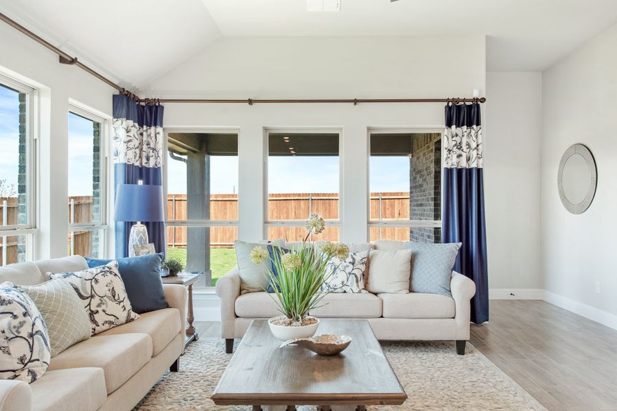Living room with two cream sofas, navy curtains, vaulted ceiling, and large windows overlooking a backyard fence.