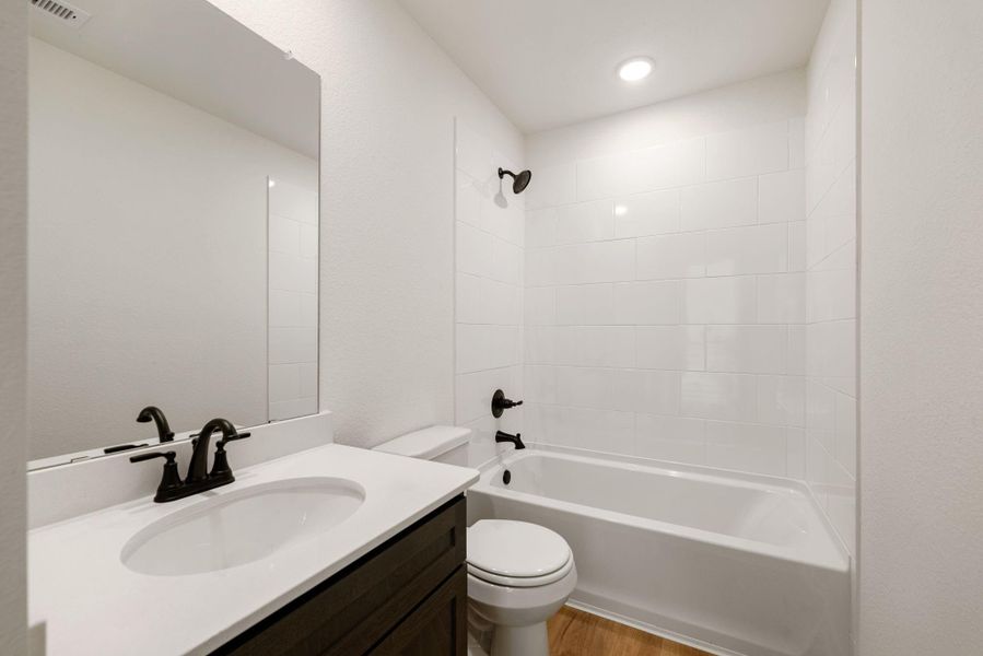 This secondary bathroom is clean, bright, and functionally designed. It features a sleek single vanity with dark cabinetry, a white countertop, and modern black fixtures for both the faucet and the tub/shower combination. A large, frameless mirror spans the width of the vanity, enhancing the sense of light and space. This secondary bathroom is clean, bright, and functionally designed. It features a sleek single vanity with dark cabinetry, a white countertop, and modern black fixtures for both the faucet and the tub/shower combination. A large, frameless mirror spans the width of the vanity, enhancing the sense of light and space.