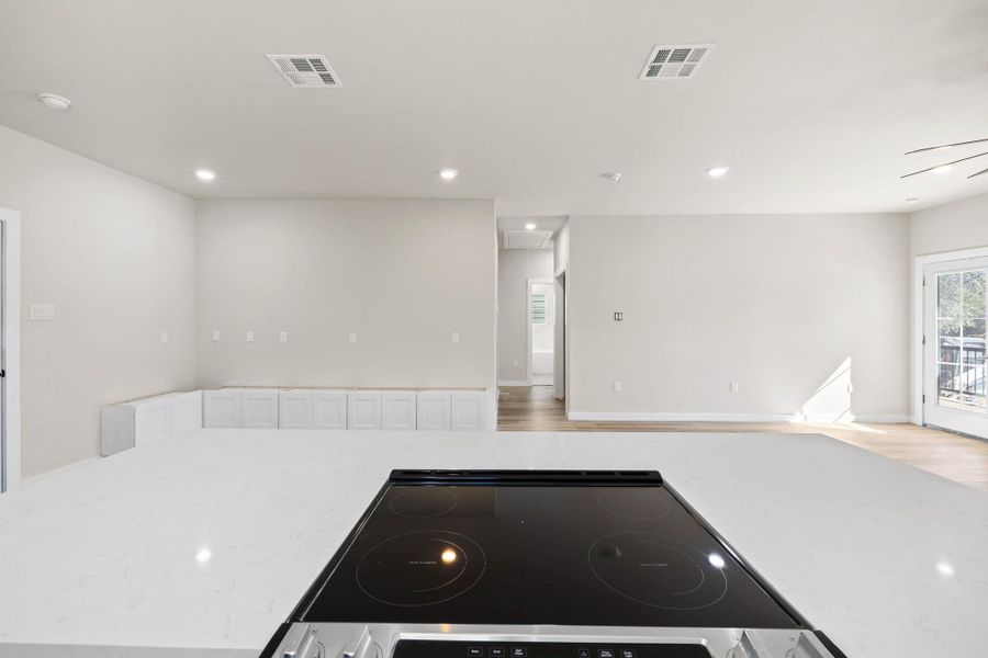 Kitchen with light stone countertops, electric cooktop, recessed lighting, open floor plan, and light wood finished floors Kitchen with light stone countertops, electric cooktop, recessed lighting, open floor plan, and light wood finished floors