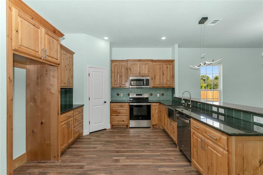 Kitchen with stainless steel appliances, backsplash, decorative light fixtures, dark wood finished floors, and a peninsula