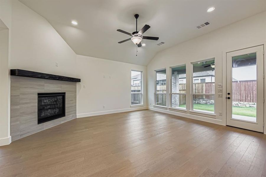 Unfurnished living room featuring light wood-type flooring, vaulted ceiling, plenty of natural light, a fireplace, and recessed lighting