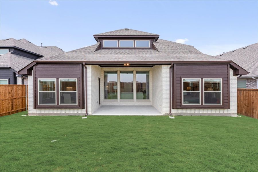Rear exterior of single-story home with covered patio, brick and dark siding, and large green backyard