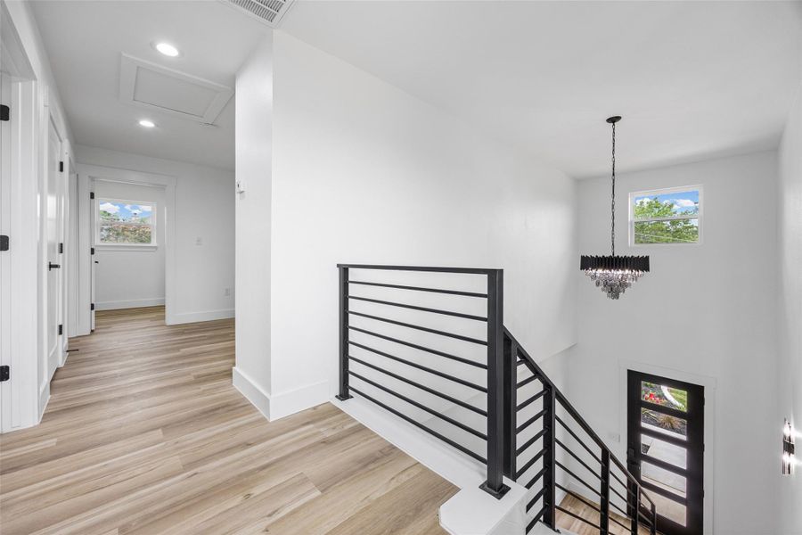 Contemporary interior featuring modern lighting, wood-finish flooring, white walls, and a modern horizontal metal stair railing Contemporary interior featuring modern lighting, wood-finish flooring, white walls, and a modern horizontal metal stair railing