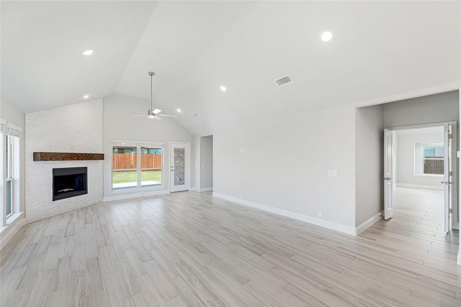 Open living room with vaulted ceiling, stone fireplace, ceiling fan, and light wood-look floors