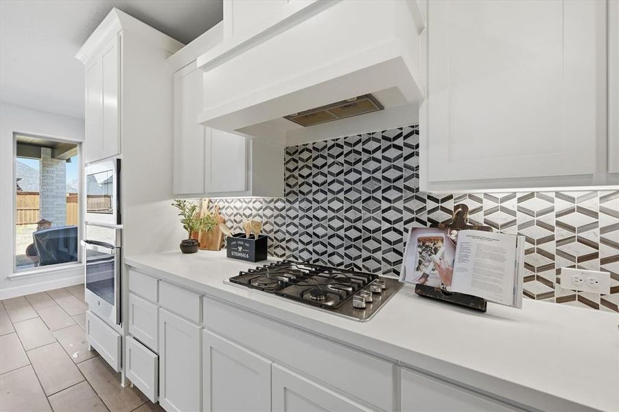Kitchen featuring white cabinetry, gas cooktop, black & white backsplash, and light stone countertops