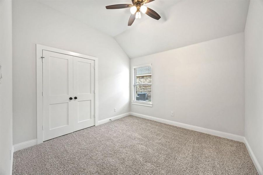 Unfurnished bedroom featuring vaulted ceiling, carpet, a closet, and a ceiling fan