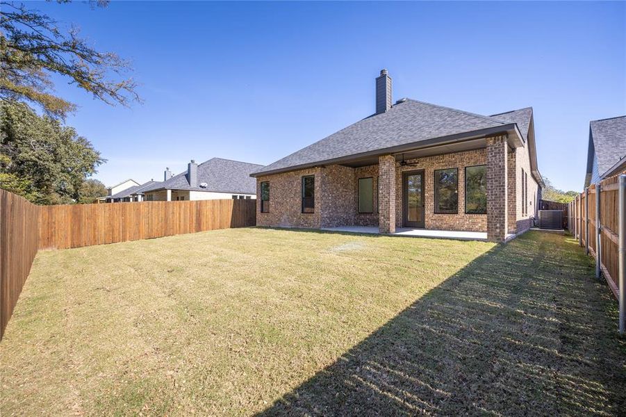 Rear view of house with a fenced backyard, a shingled roof, a patio, a chimney, and brick siding