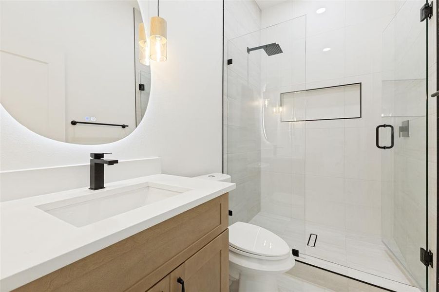 Contemporary bathroom featuring a light wood-finish vanity with a white integrated sink and countertop, black matte faucet, and round backlit mirror Contemporary bathroom featuring a light wood-finish vanity with a white integrated sink and countertop, black matte faucet, and round backlit mirror