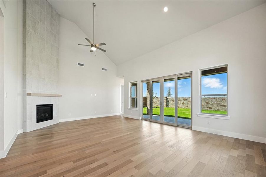 Unfurnished living room with high vaulted ceiling, light wood-style flooring, a tile fireplace, ceiling fan, and recessed lighting Unfurnished living room with high vaulted ceiling, light wood-style flooring, a tile fireplace, ceiling fan, and recessed lighting
