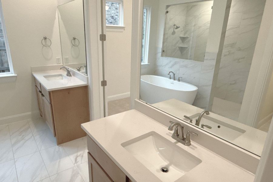 Full bath with light marble finish flooring, two vanities, a freestanding tub, and a marble finish shower