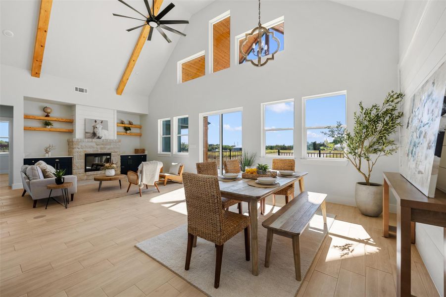 Dining space with high vaulted ceiling, a stone fireplace, light wood finished floors, beamed ceiling, and ceiling fan