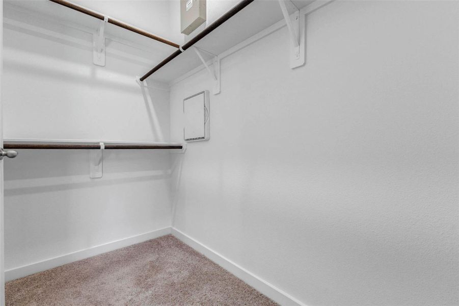 Walk-in closet with built-in hanging rods, upper shelving, and soft carpet underfoot. This storage space provides practical organization for clothing, shoes, accessories, and everyday essentials within the primary suite.