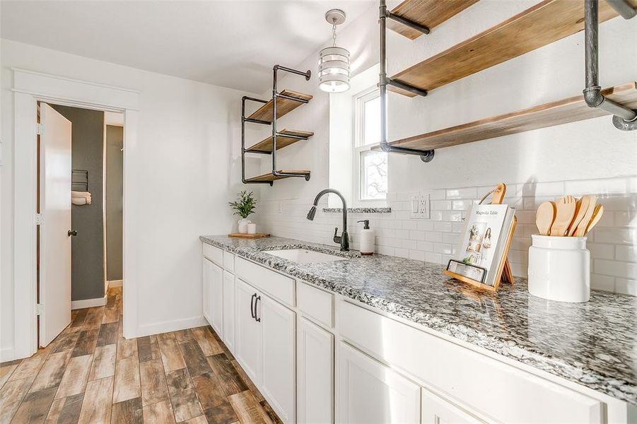 Kitchen with open shelves, light stone counters, light wood finished floors, white cabinetry, and backsplash