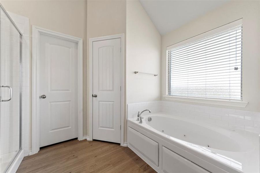 Bathroom with wood-type flooring, vaulted ceiling, and plus walk in shower