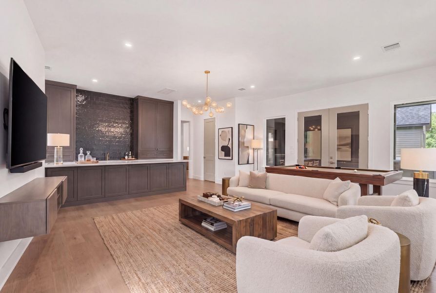 Bright, oversized gameroom with clean modern finishes and walls of windows bringing in natural light and backyard views. French doors open directly to the covered back patio, creating an easy indoor-outdoor setup. The built-in wet bar with beverage refrigerator keeps drinks and snacks within reach, making this space ready for game nights.Statement wet bar in the gameroom featuring custom wood cabinetry, brass hardware, and a bold full-height tile backsplash that adds depth and texture.