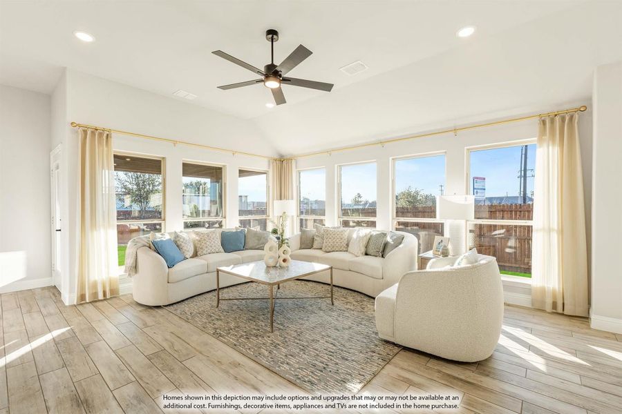 Bright living room with curved white sofas, wood-look floors, ceiling fan, and large windows with sheer curtains Bright living room with curved white sofas, wood-look floors, ceiling fan, and large windows with sheer curtains