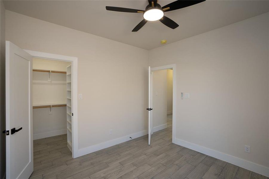 Unfurnished bedroom featuring ceiling fan, a spacious closet, a closet, and light wood-type flooring