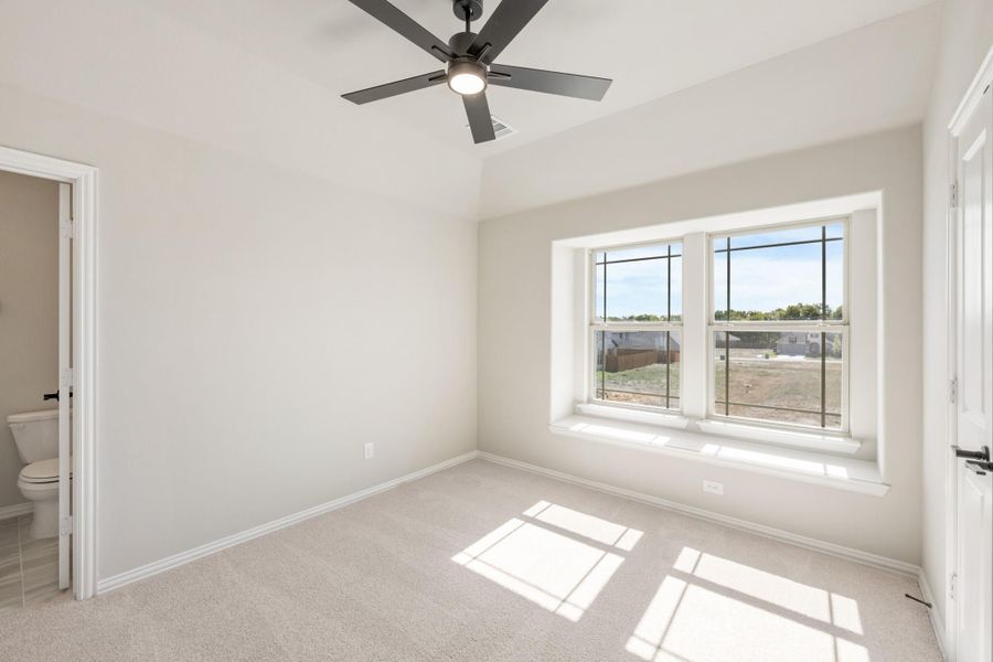 Empty bedroom with carpet, ceiling fan, large window, and adjoining bathroom door visible Empty bedroom with carpet, ceiling fan, large window, and adjoining bathroom door visible