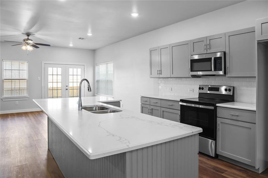 Kitchen with gray cabinets, an island with sink, and appliances with stainless steel finishes