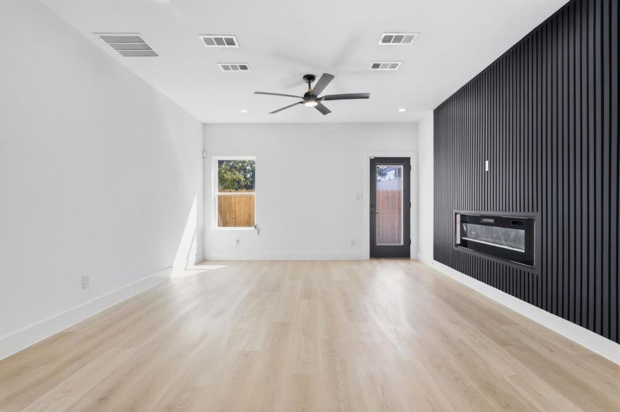 Spacious interior with light wood-finish flooring, a contemporary black slat accent wall, and a built-in linear fireplace Spacious interior with light wood-finish flooring, a contemporary black slat accent wall, and a built-in linear fireplace