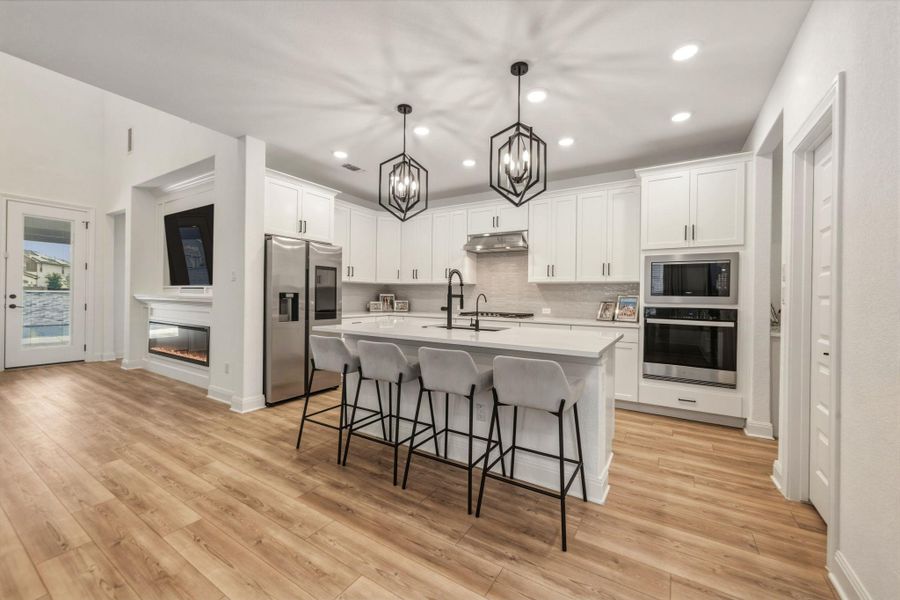 Spacious kitchen featuring white cabinetry, stainless steel appliances, a center island with seating, pendant lighting, and quartz countertops