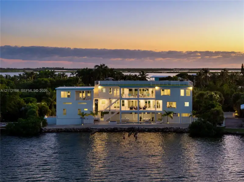 Waterfront residence featuring multi-level balconies, expansive glass windows, a flat roofline, and a private dock Waterfront residence featuring multi-level balconies, expansive glass windows, a flat roofline, and a private dock