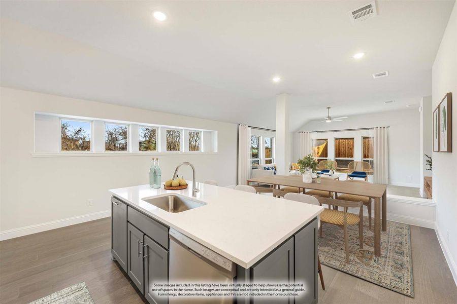Kitchen island with gray cabinets and white countertop, open to dining area with hardwood floors and clerestory windows.